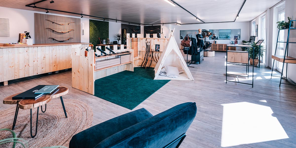BEARPAW Store Rossach – Moderner Innenraum mit Holzdesign, Ausstellungsfläche für Bögen, einem Zelt für Kinder und einer grünen Sitzecke für Besucher nahe Coburg.