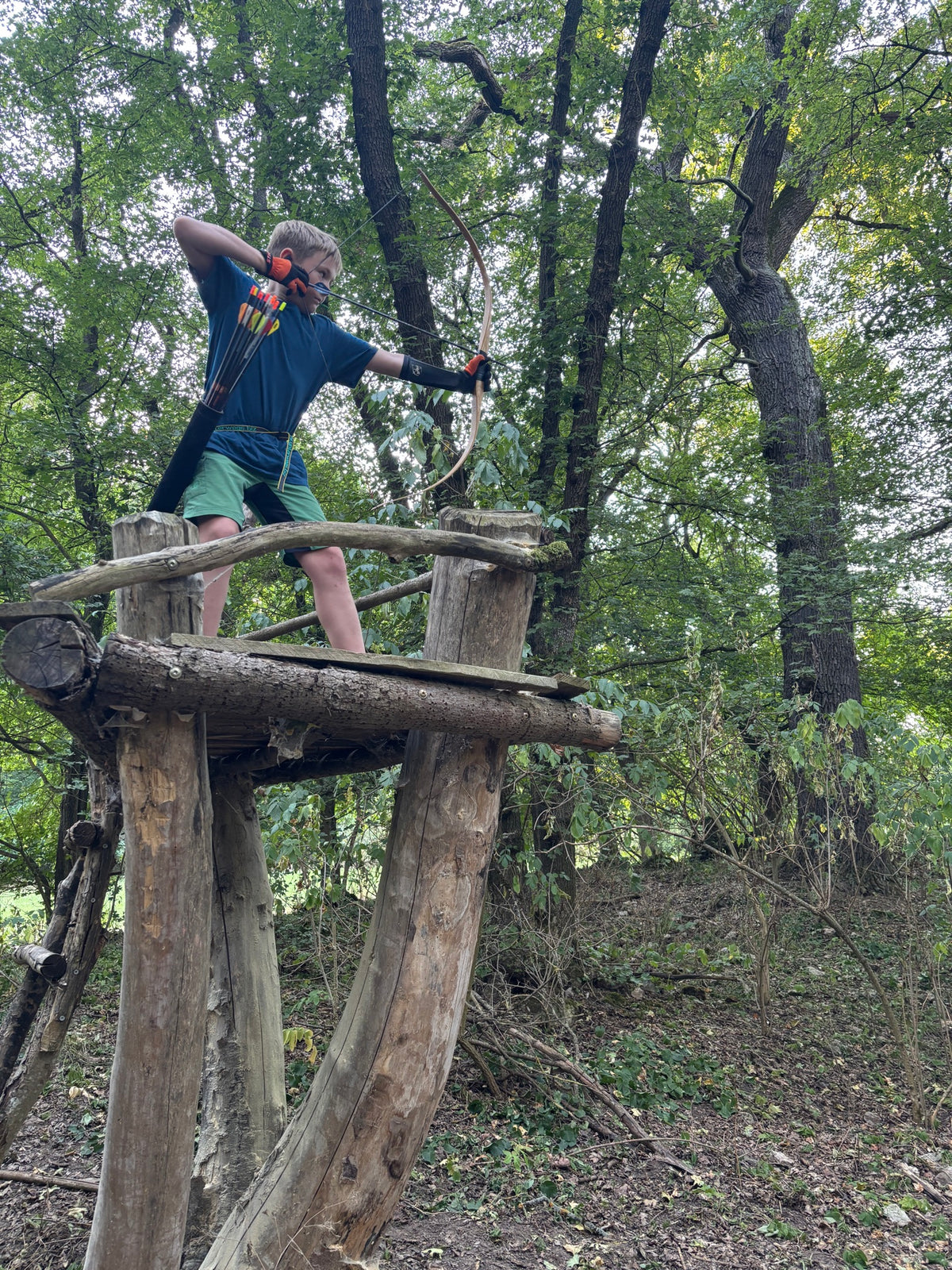Junge mit Langbogen auf einer Holzplattform im Wald